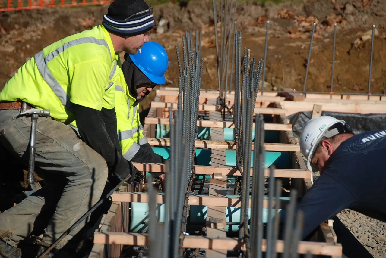 Construction workers assembling wooden forms and rebar for a concrete foundation at House 432.