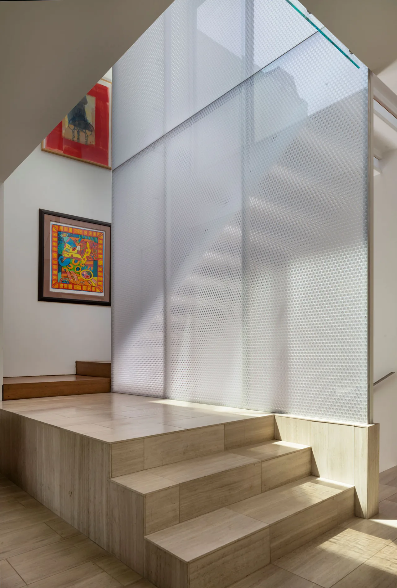 Wood-clad stairs next to a large translucent textured glass wall in a modern interior space.