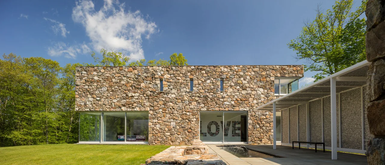 House 432 by Robert Siegel Architects features a stone facade, flat roof, and large glass windows in a woodland setting.