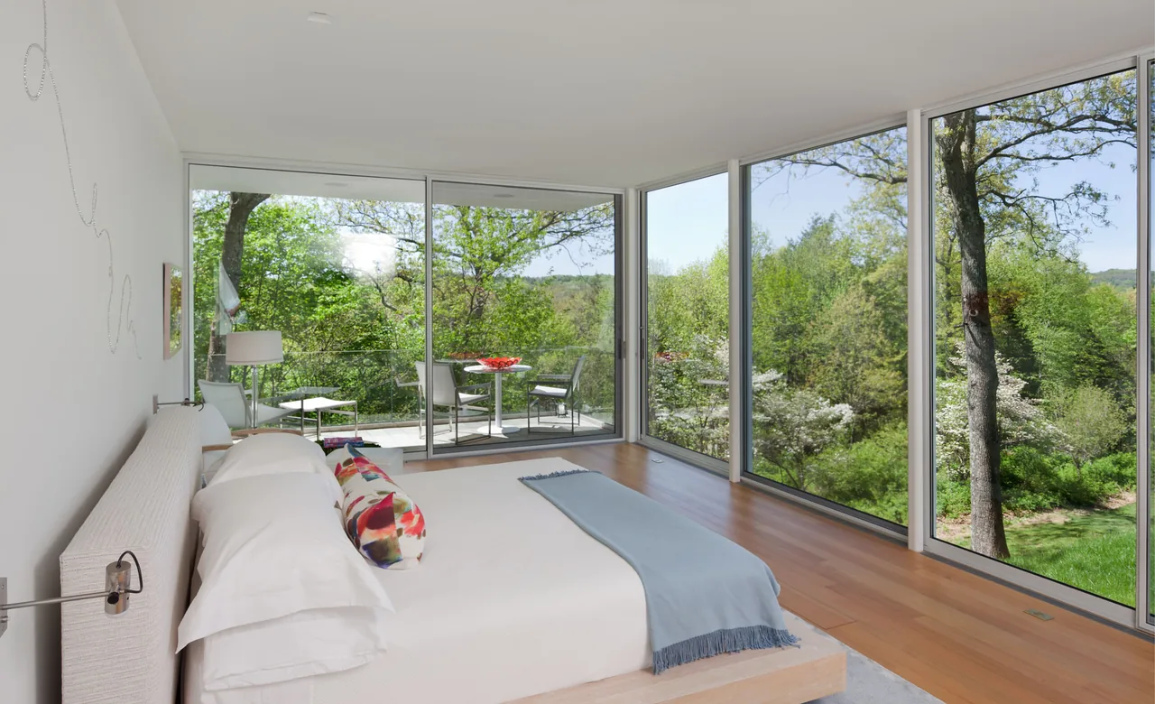 House 125 bedroom features floor-to-ceiling glazing with sliding glass door access to a balcony overlooking greenery.