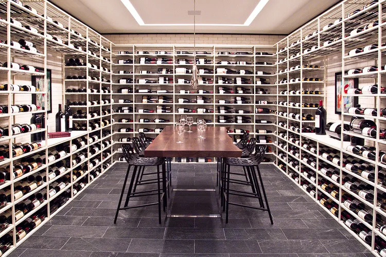 Wine cellar with extensive wall-mounted wine racks, a central wooden table, and seating for wine tasting or gathering.