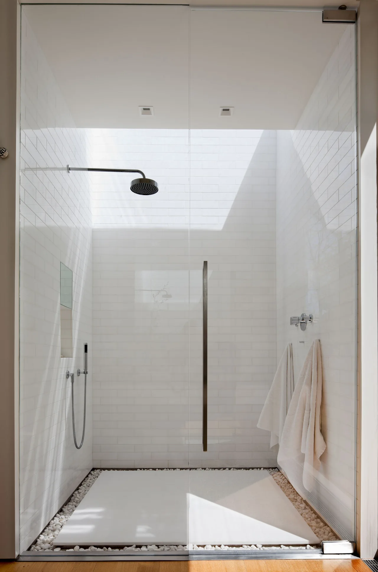 A walk-in shower features white brick-style tiles, a rain showerhead, and white towels on a wall-mounted hook.