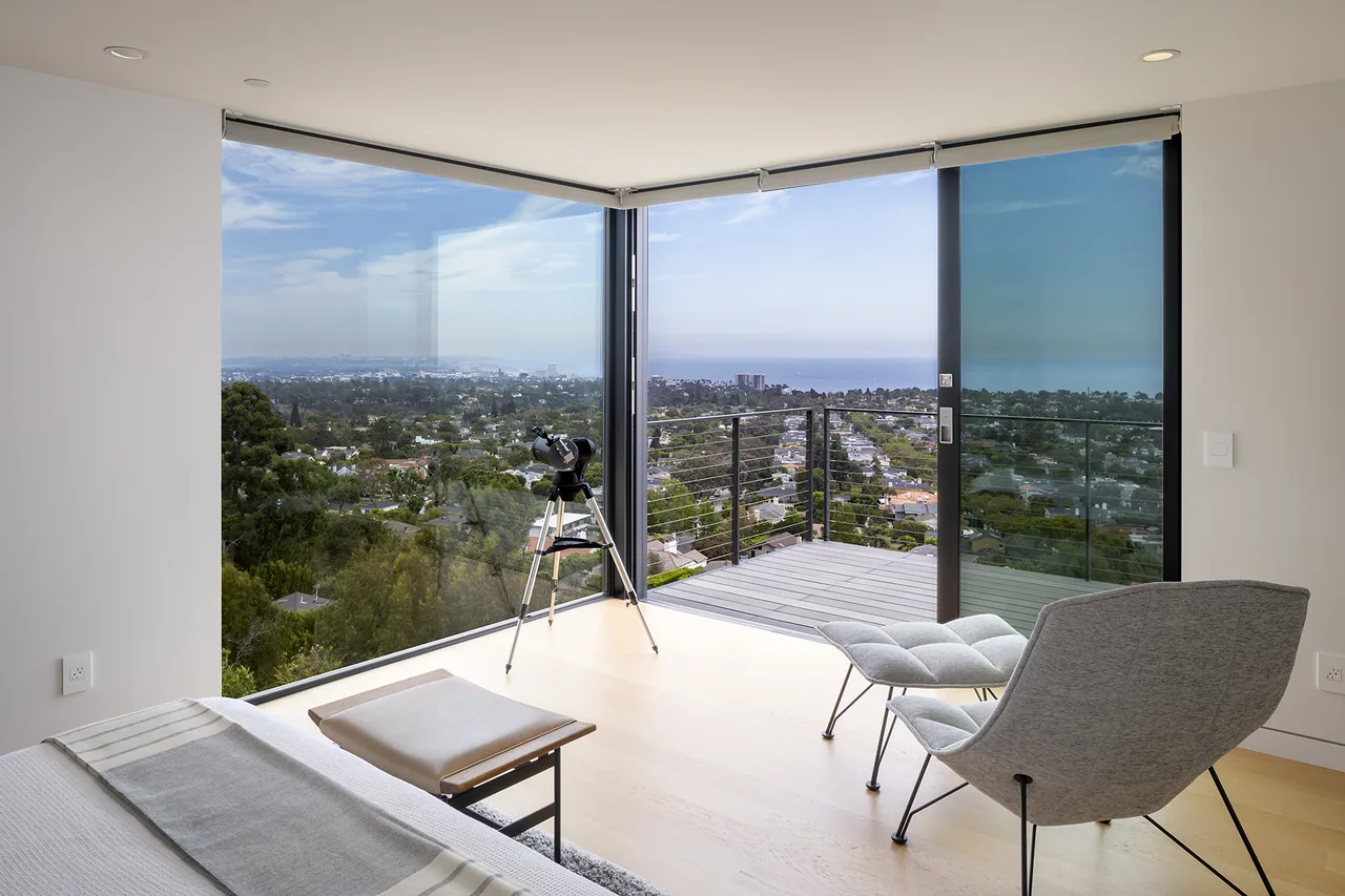 Bedroom with floor-to-ceiling glazing offers an ocean view and access to a balcony with metal railing.