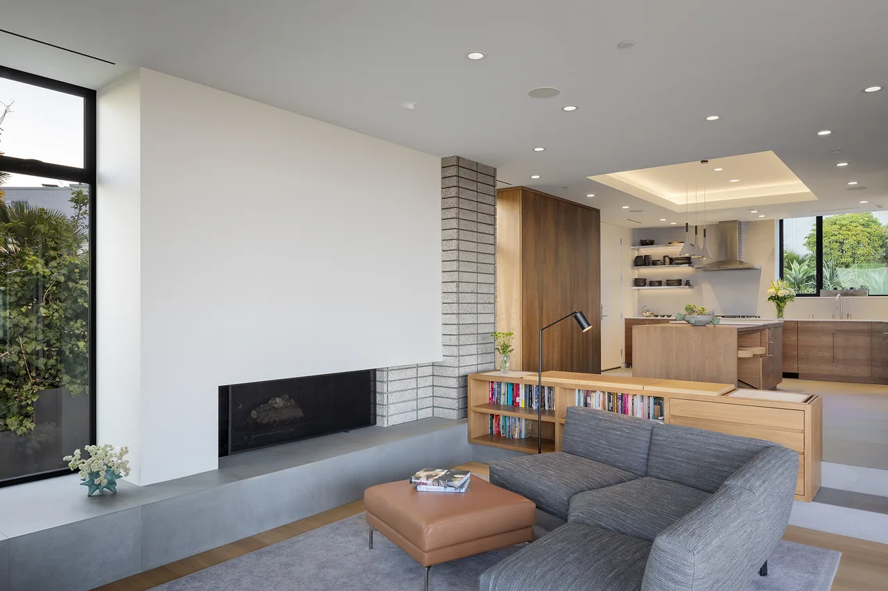 Living area with a built-in fireplace, gray sofa, and open kitchen with wood cabinetry in the background.