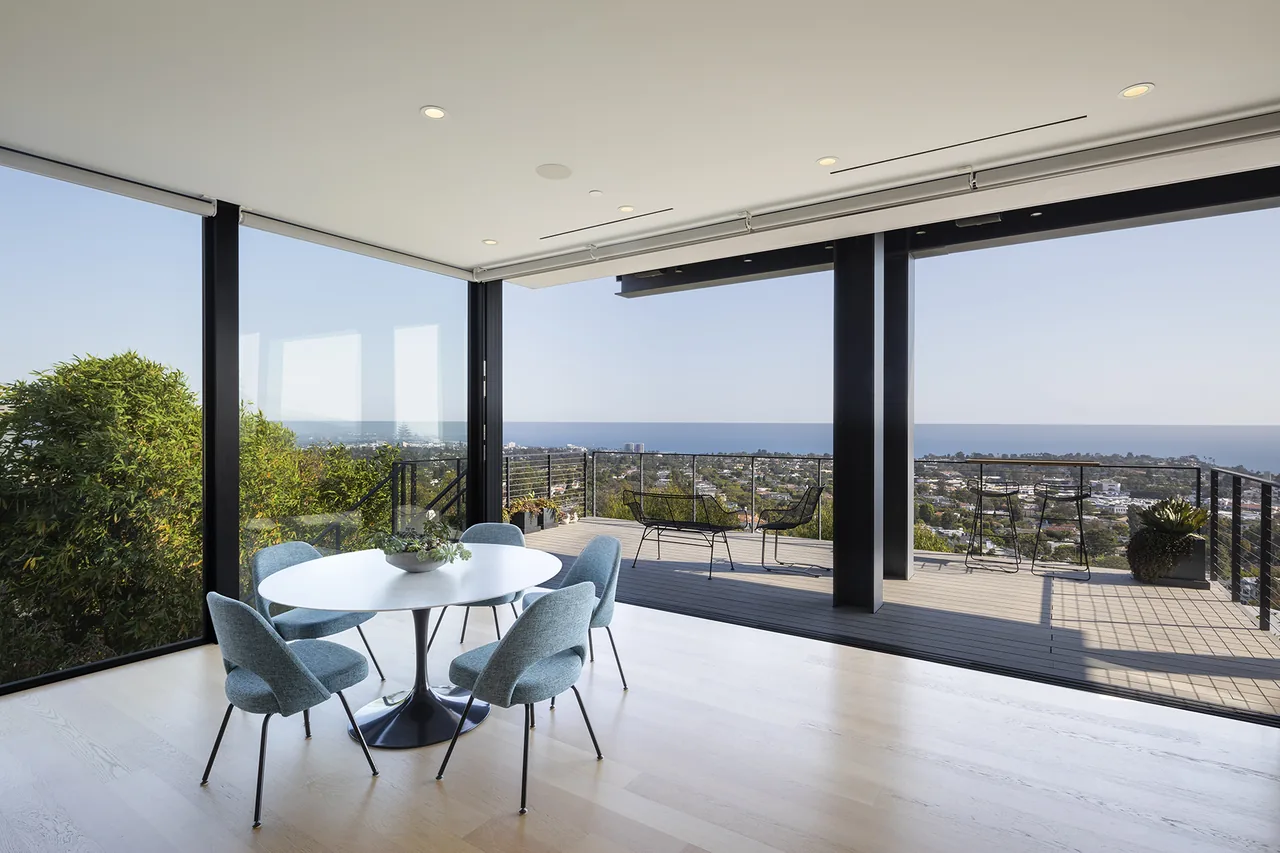 Dining space with floor-to-ceiling glazing opens to an outdoor deck overlooking a coastal view.