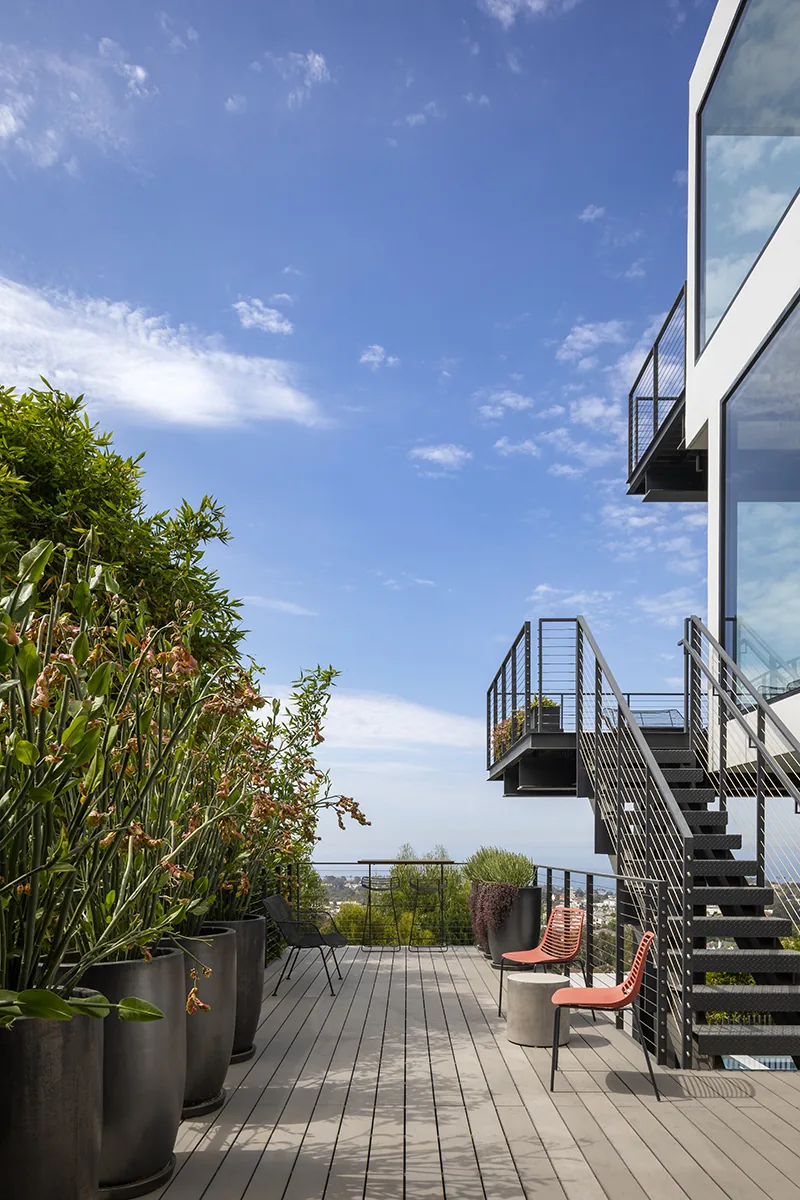 Outdoor living space on a modern home features metal stairs, wire railing, and potted plants with city views.