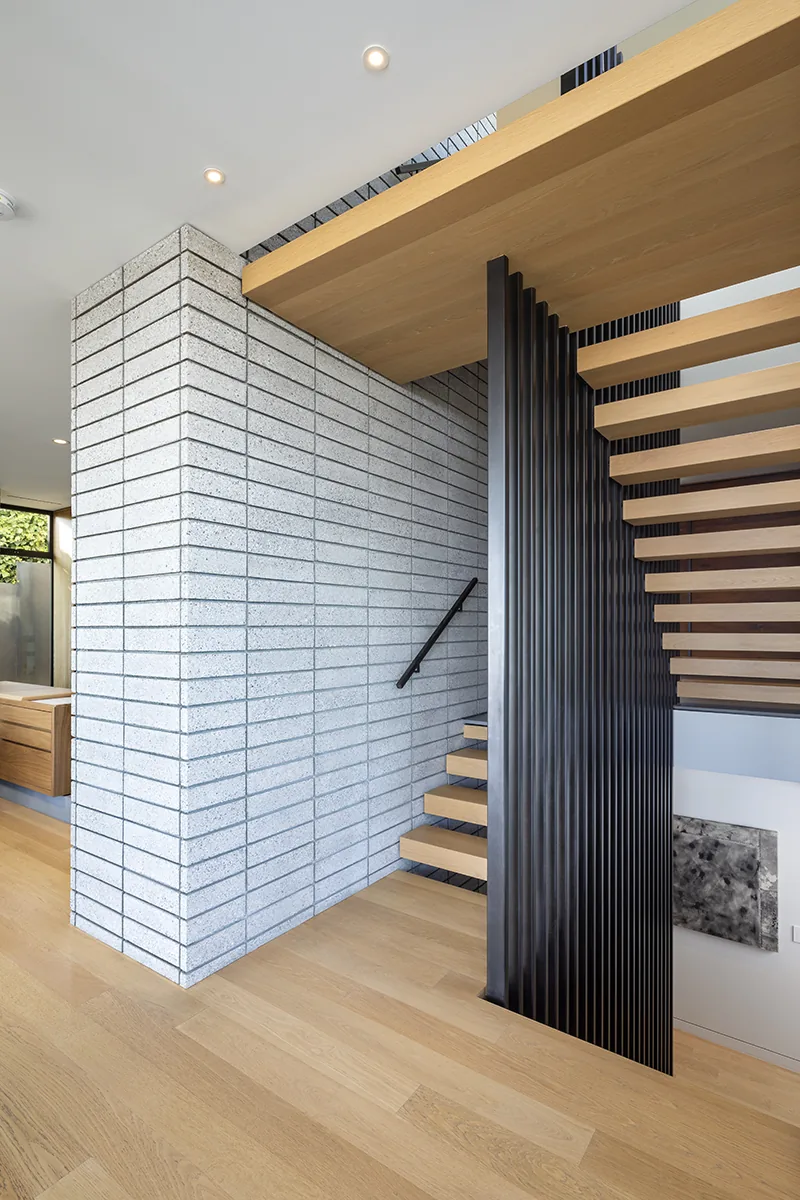 Modern staircase with wood treads and black vertical balusters next to a gray brick wall in a home.