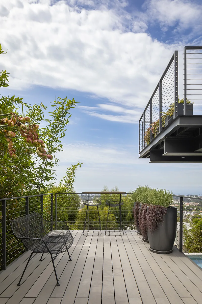 Outdoor modern deck at Palisades House features metal cable railings and seating with hillside and city views.