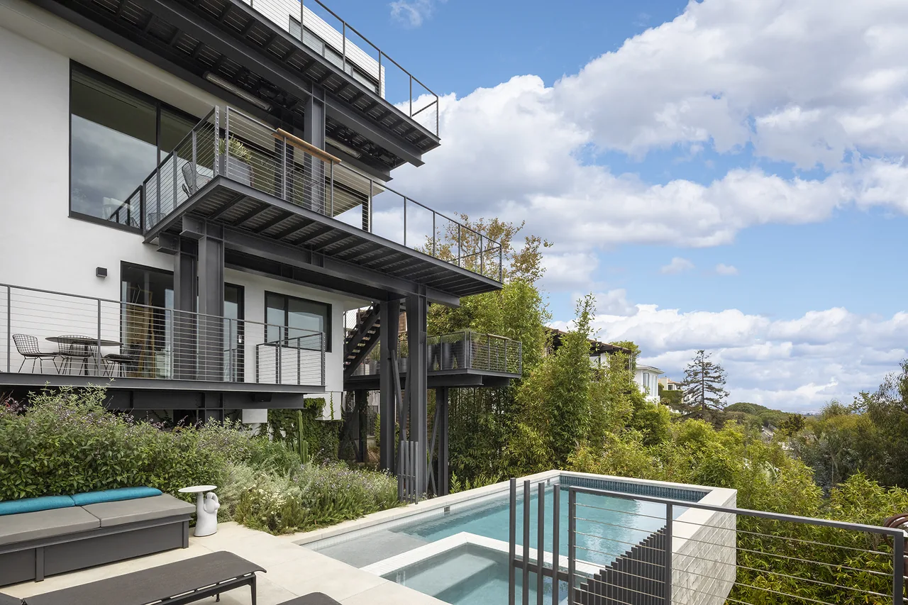 The Palisades House features metal balconies with cable railings and a compact pool surrounded by lush greenery.