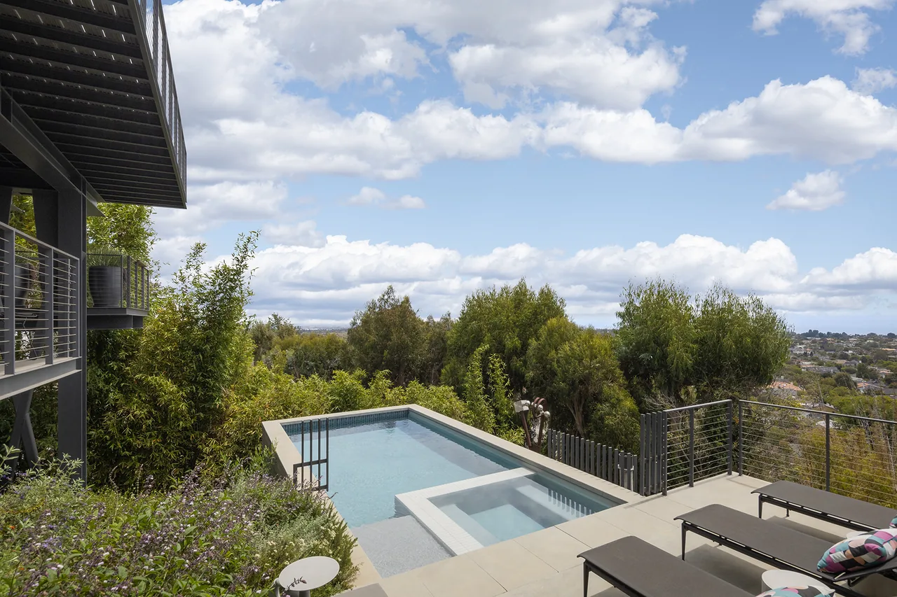Palisades House features metal cable railings on balconies overlooking a pool and city views with lush landscaping.