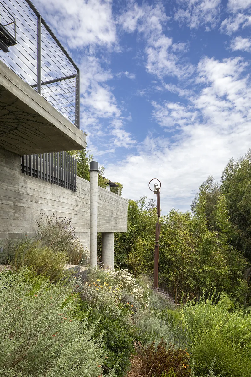 The Palisades House features a concrete balcony with metal cable railing surrounded by dense landscaping.