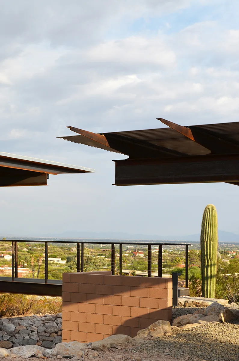 Detail of the DWC House featuring corrugated metal roofing, metal beams, and cable railings overlooking desert surroundings.