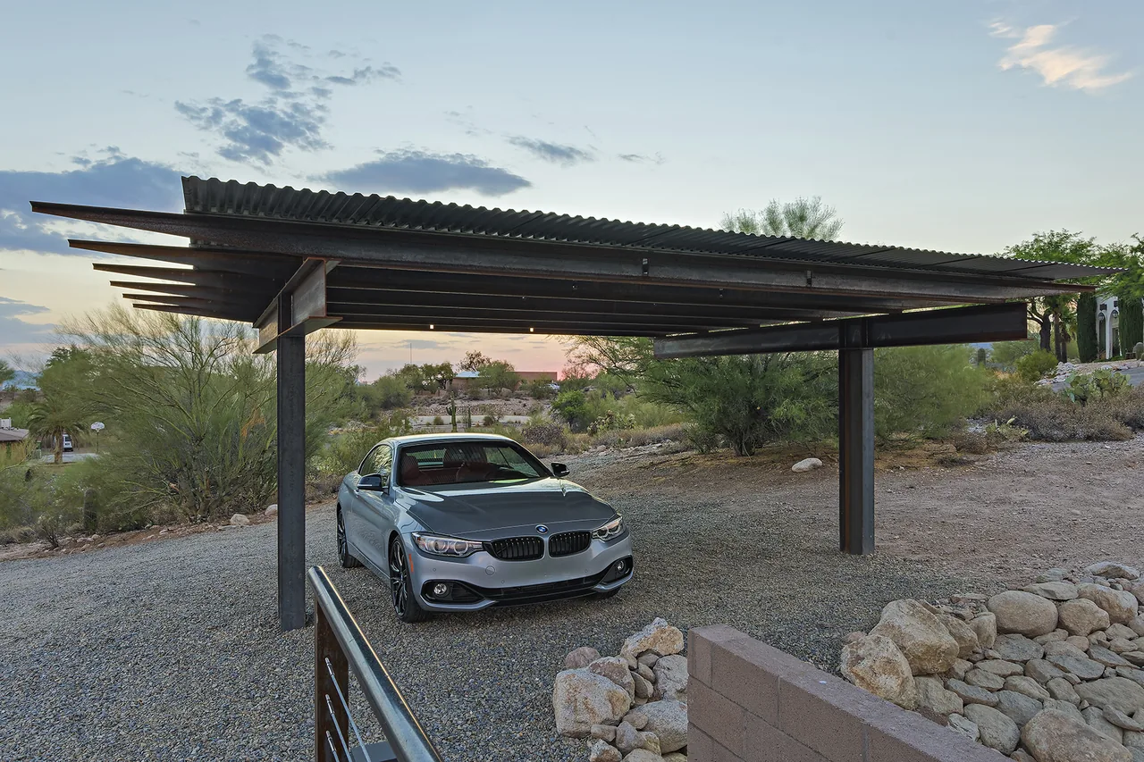 The DWC House features a carport with a corrugated metal roof supported by black steel posts.
