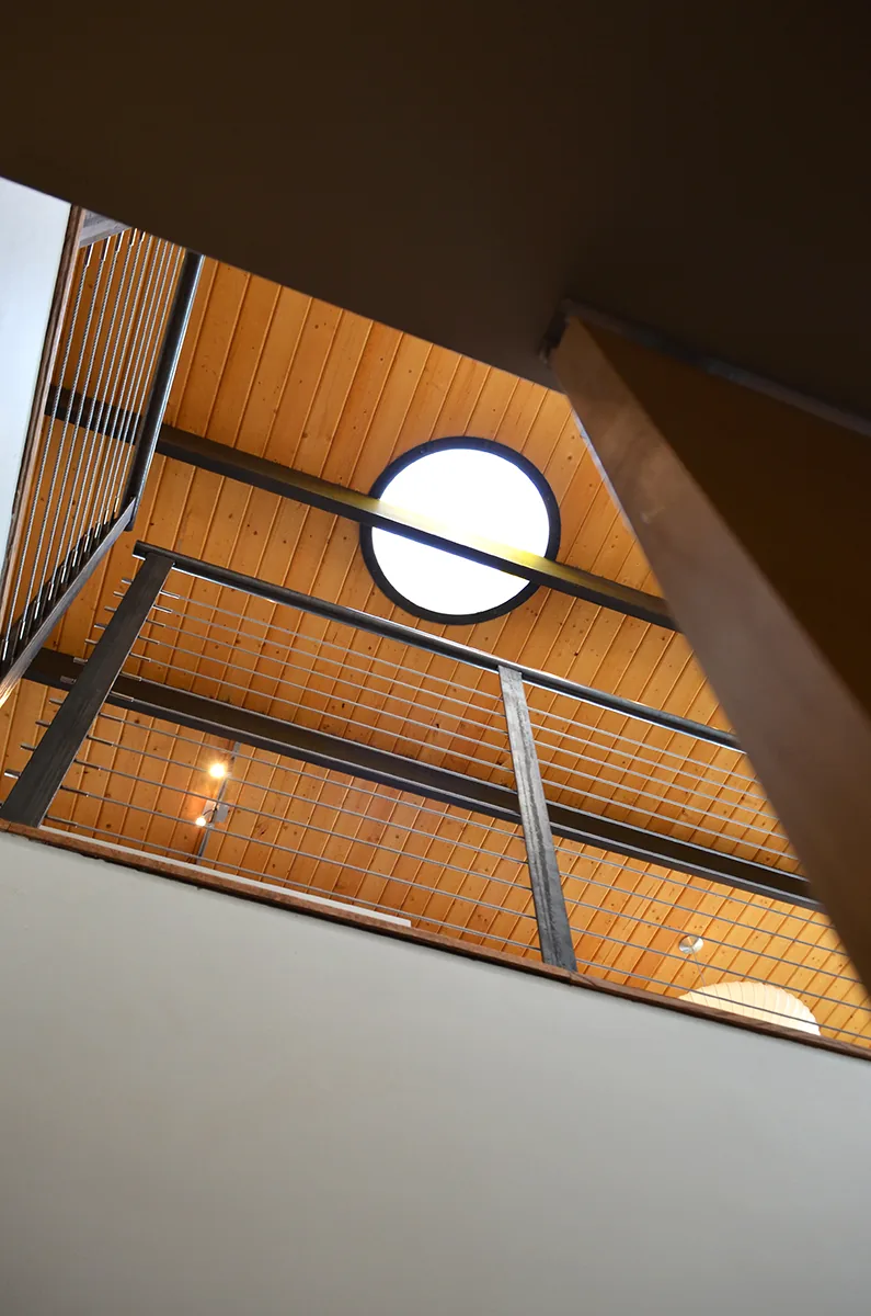 DWC House features a circular skylight above a wood-paneled ceiling and metal cable railing.