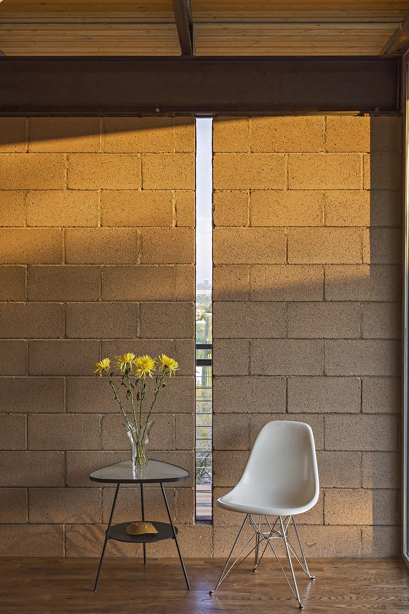Narrow vertical window in a concrete block wall with a white chair and side table inside the DWC House.