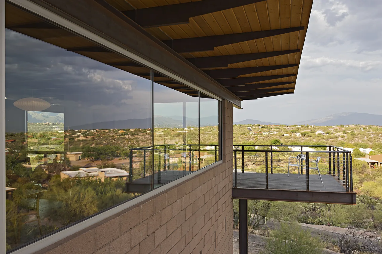 Cantilevered balcony with metal railing extends from a desert home offering views of the surrounding landscape.