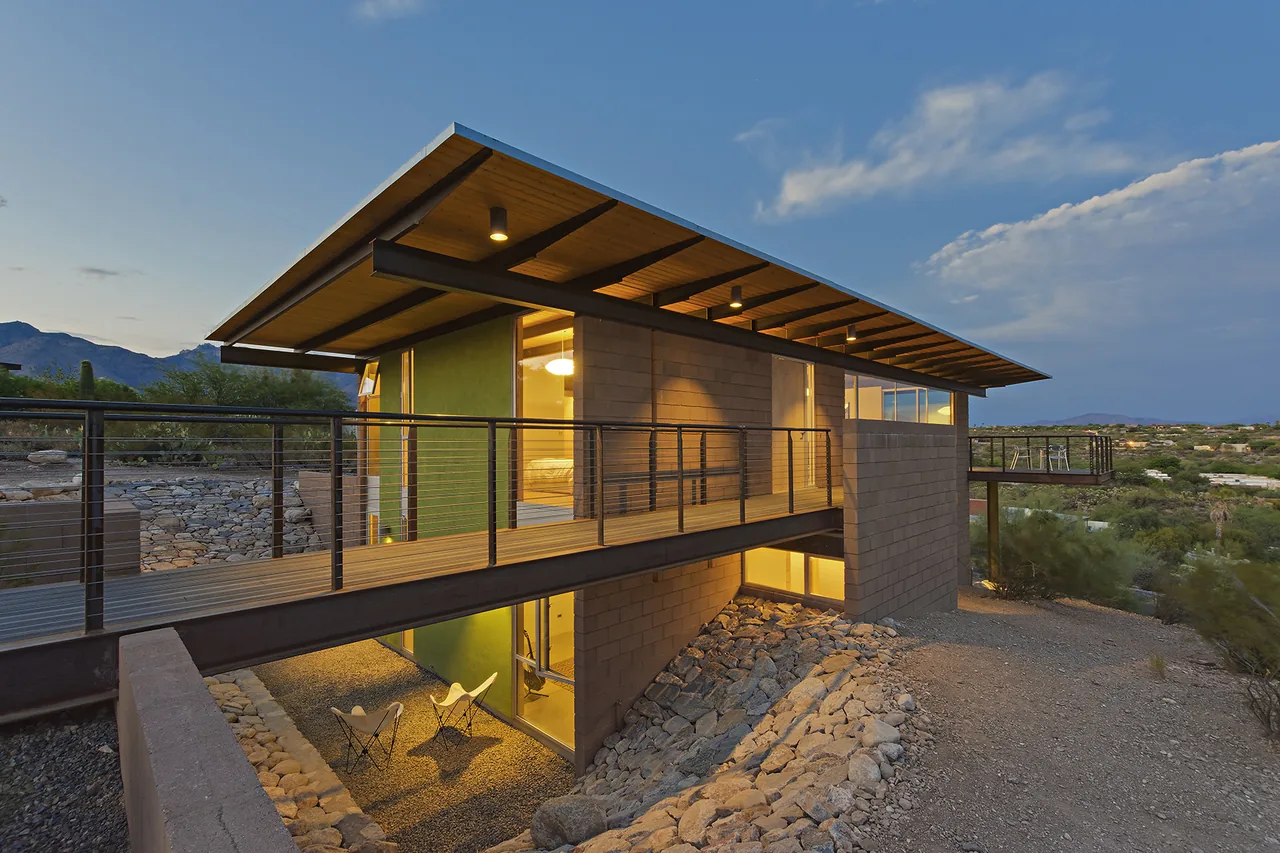 The DWC House features a cantilevered walkway and flat roof with exterior lighting in a desert setting at dusk.