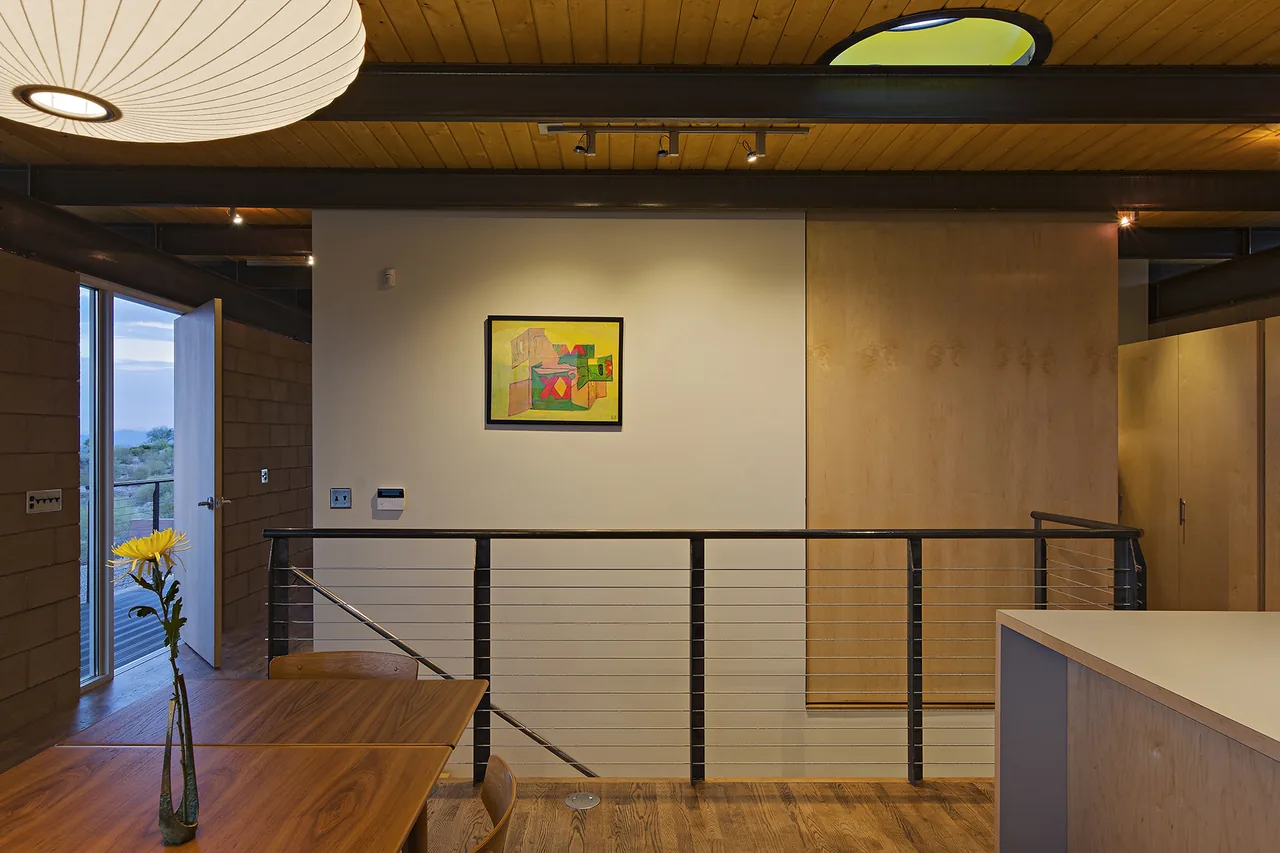 Dining area in DWC House showing wood ceiling, cable railing, and a door with desert views outside.