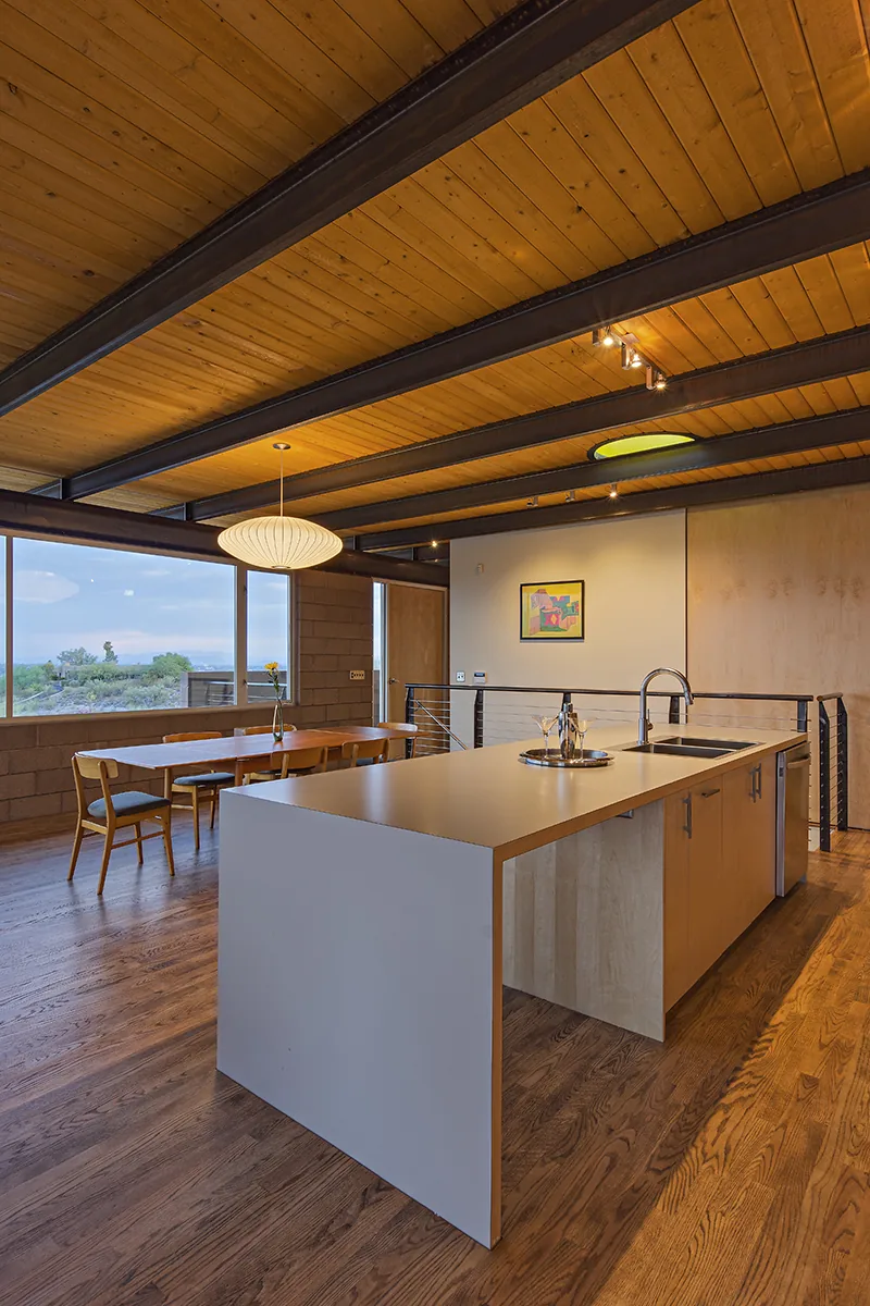 Open kitchen and dining space features exposed wood ceiling planks and a large kitchen island with a modern faucet.