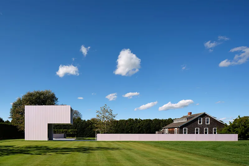 The Pink House project features a modern pink building and fence contrasting with a traditional house on a spacious lawn.