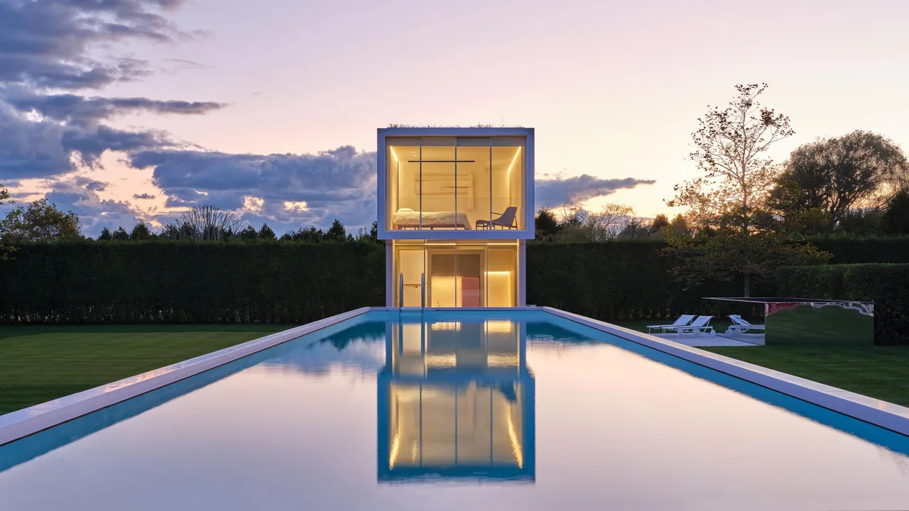 The Pink House pool house features minimalist design with large glass walls and a rectangular pool reflecting the structure at sunset.