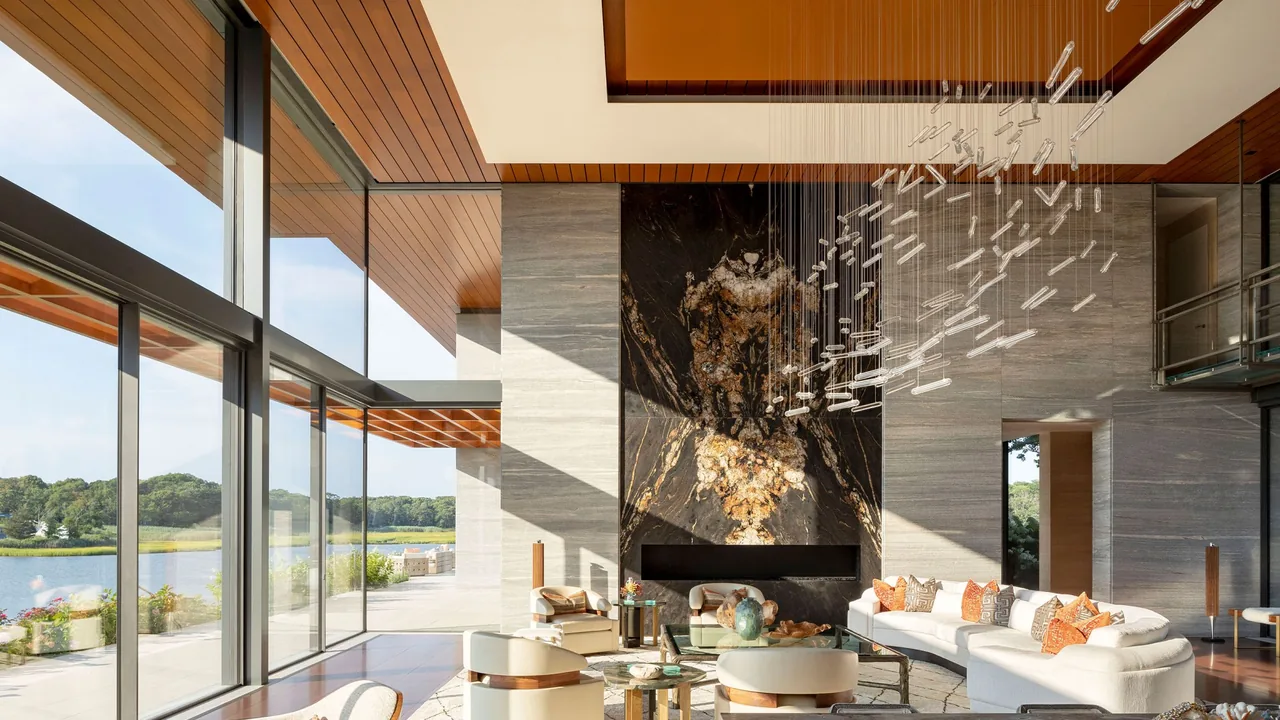 The Millstone living room features floor-to-ceiling glazing, a dramatic stone fireplace, and a large modern sculptural chandelier with views of the landscape outside.