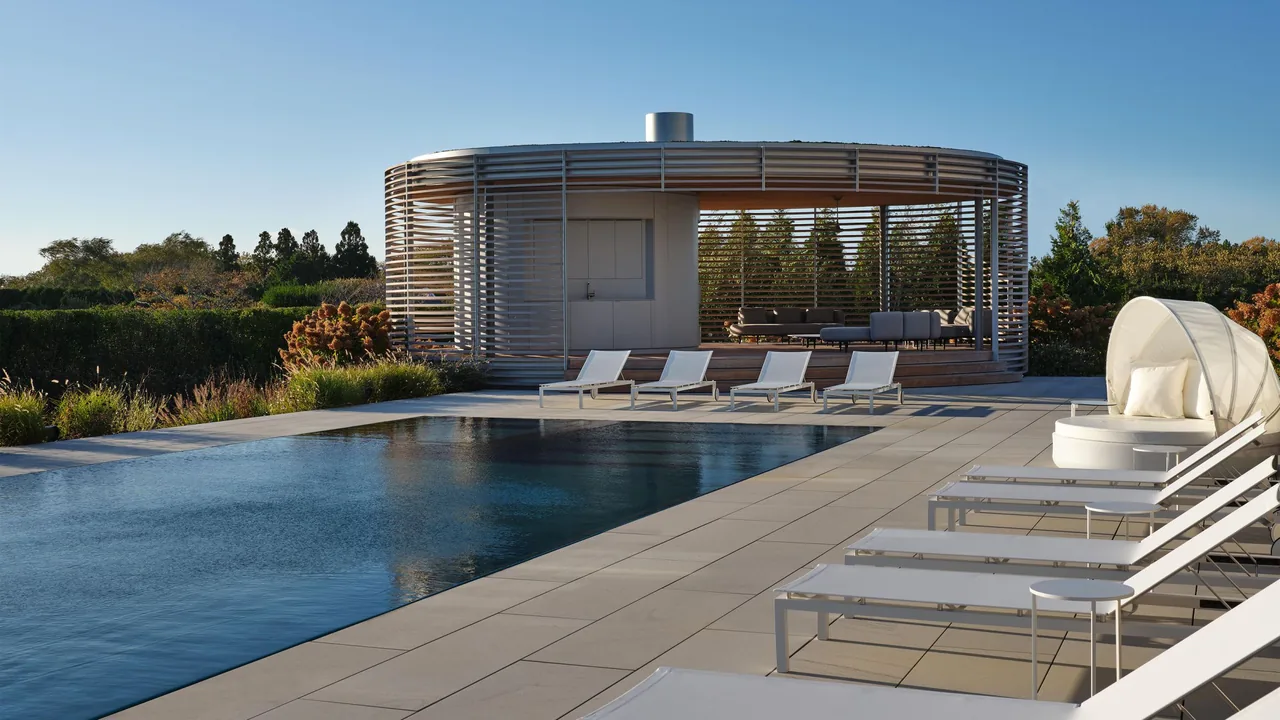 Outdoor pool area with multiple white lounge chairs and a circular pavilion screened with wooden slats.