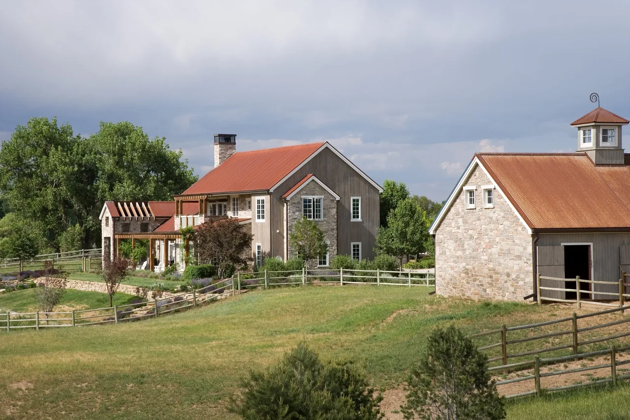 Creekside Compound features a two-story residence and a barn with red metal roofs and fenced pasture.