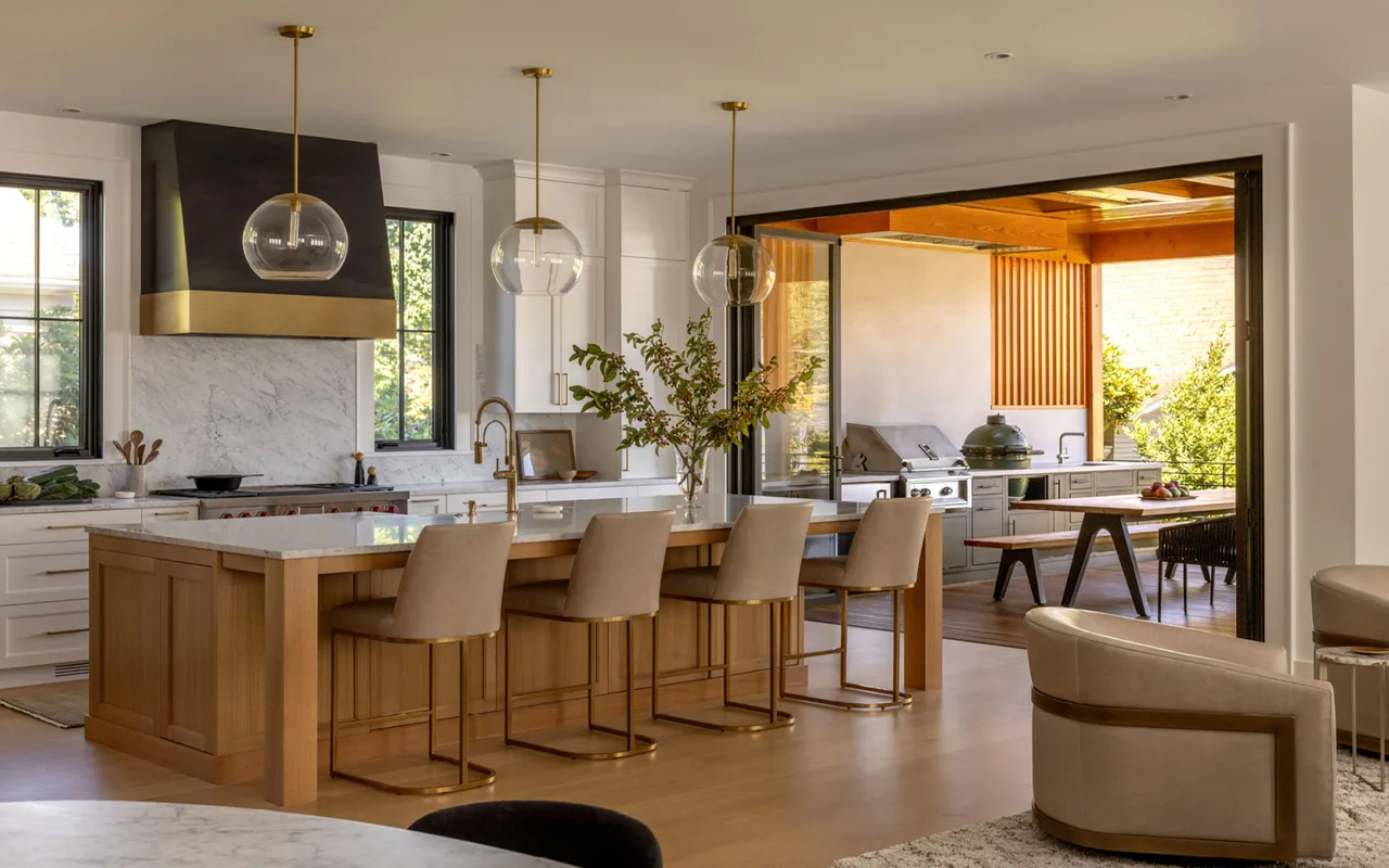This Queen Anne Transitional kitchen features a wooden island, brass pendant lights, and a seamless transition to an outdoor cooking space.