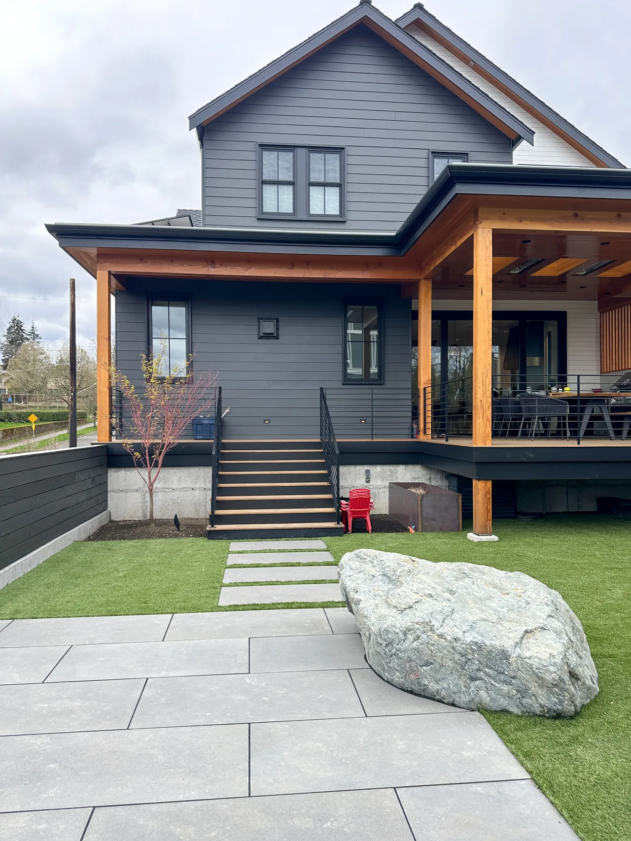 The rear exterior of the Queen Anne Transitional project in Seattle shows mixed siding colors, concrete stairs, and a covered porch with wood beams.