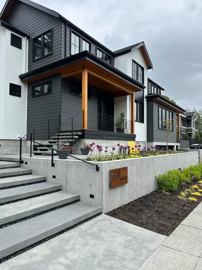 Exterior view of a modern transitional home with mixed siding colors, black framed windows, and a covered porch supported by wooden posts.