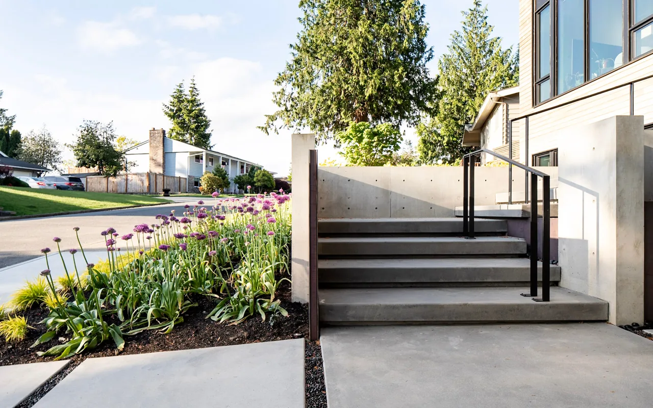 Concrete steps next to a raised planting bed with purple allium flowers and a black metal handrail.