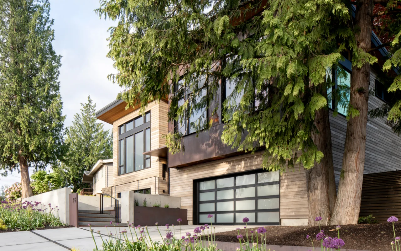 Bellevue Split-Level by Ryan Rhodes Designs shows a split-level home with horizontal wood siding and frosted glass garage door.
