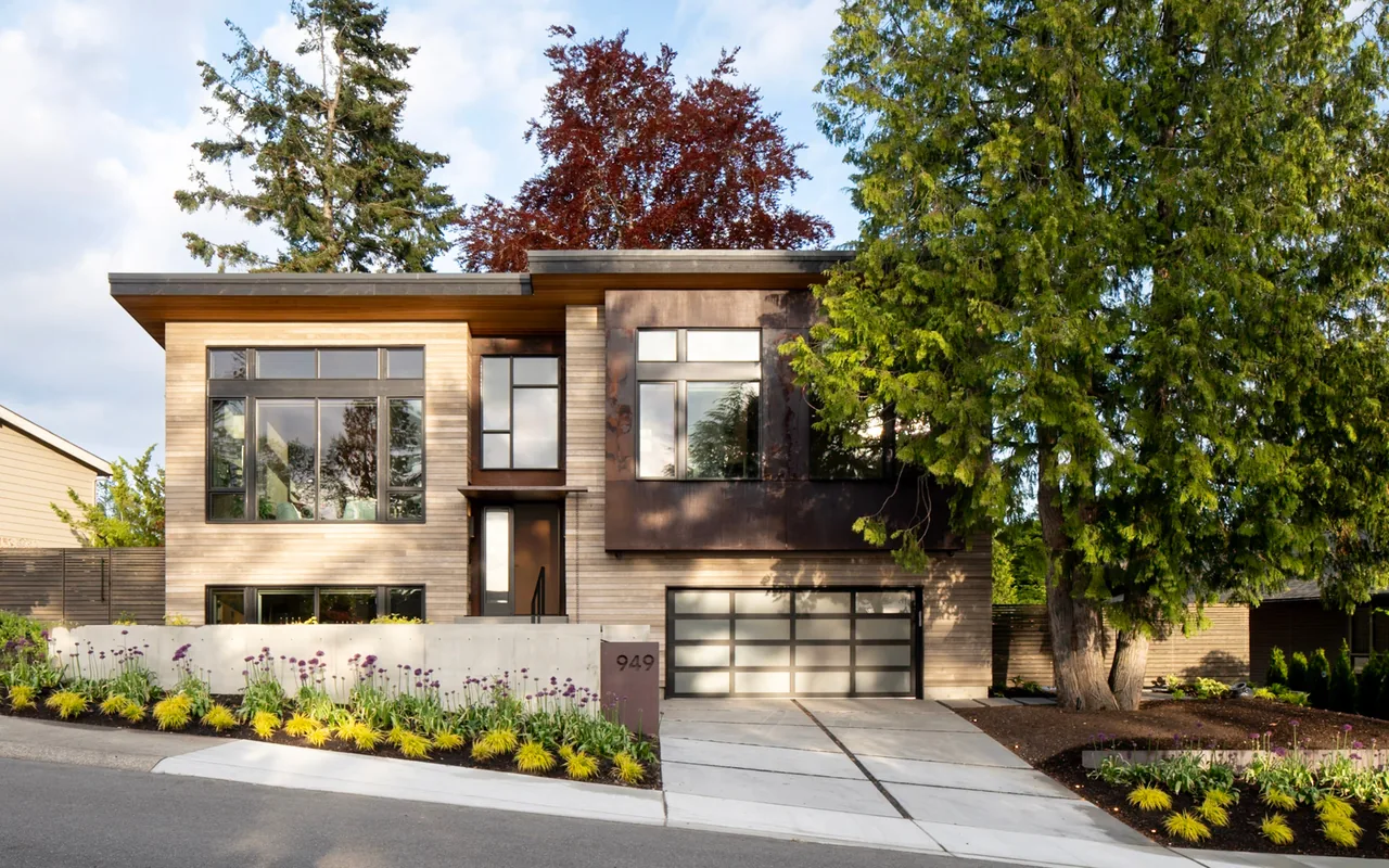 The Bellevue Split-Level features wood siding, large windows, a concrete driveway, and raised planting beds in the front yard.