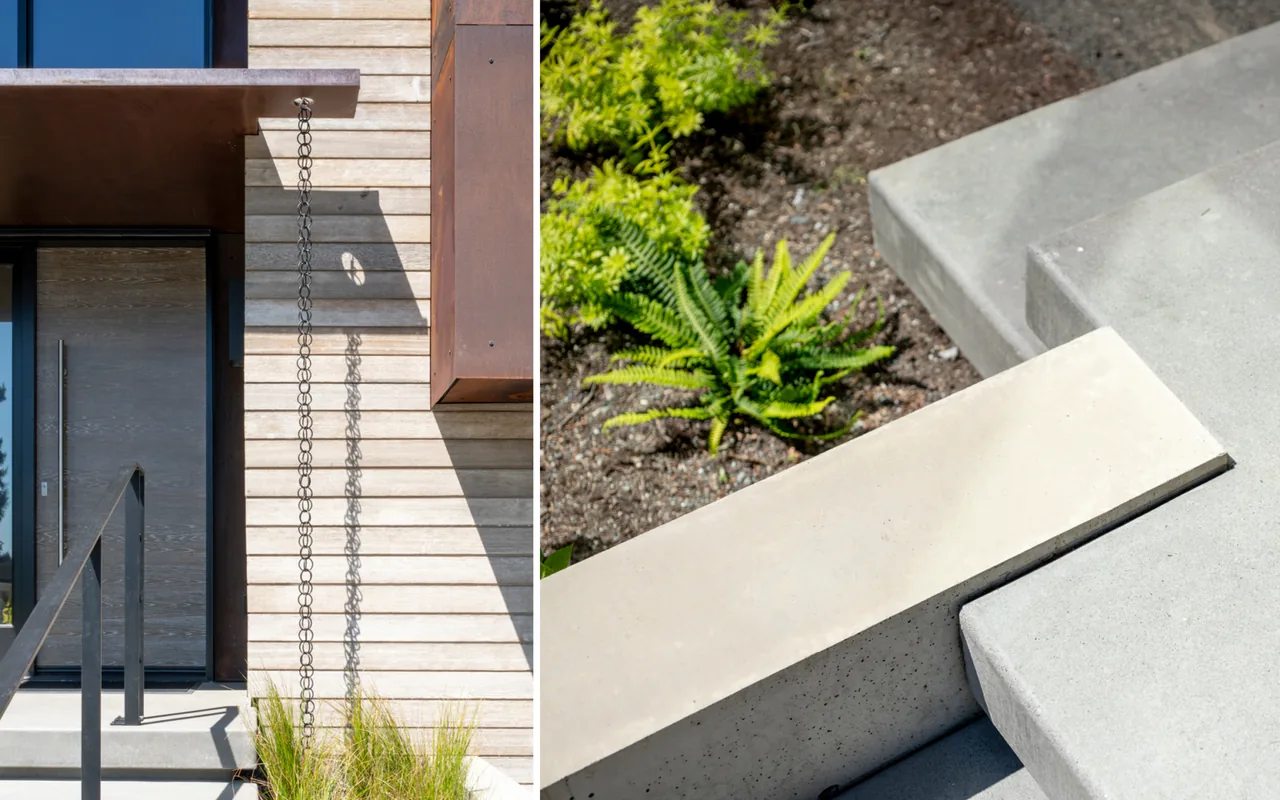 Concrete steps with black metal handrail lead to a front door with wood siding and a metal rain chain on the wall.
