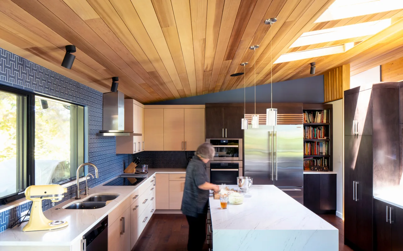 Kitchen with wood ceiling, blue accent tile backsplash, white and dark cabinetry, and a large island with pendant lighting.