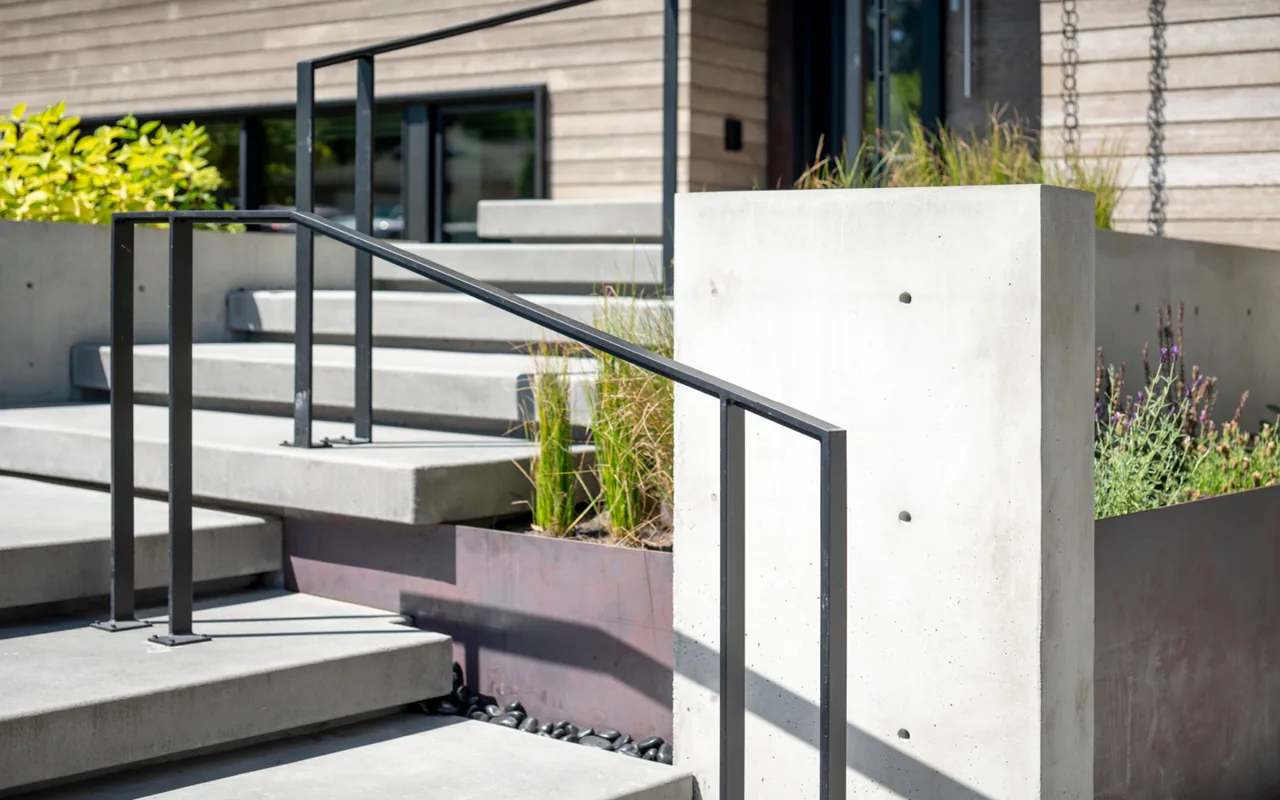 Concrete steps with a black metal railing and raised planting beds flank the entrance of a split-level house.