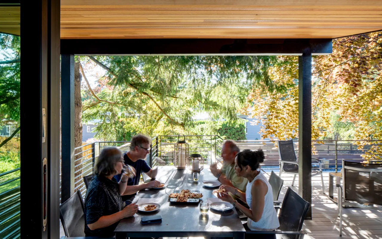 Outdoor dining area on a covered deck with a metal railing and forested views at Bellevue Split-Level project.