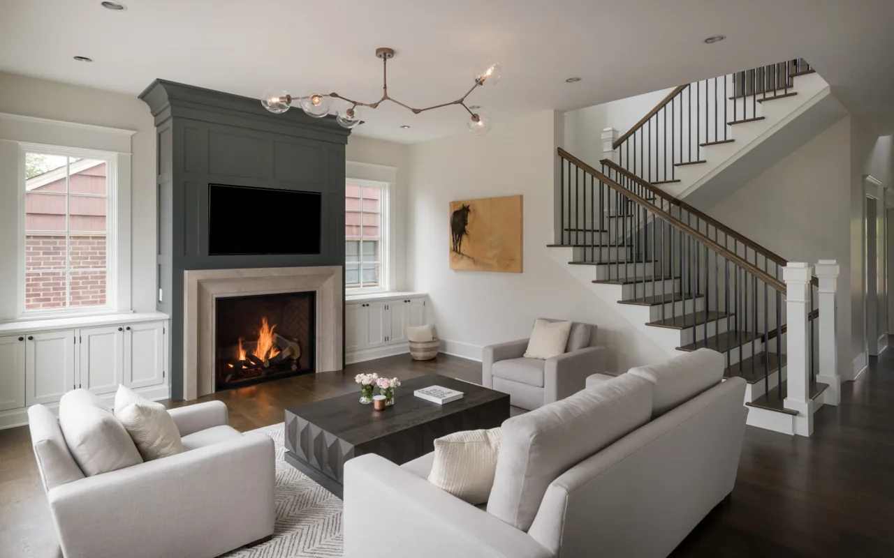 The Queen Anne Residence living room features a fireplace with TV above, white built-in cabinets under windows, and a seating area with neutral-toned furniture.