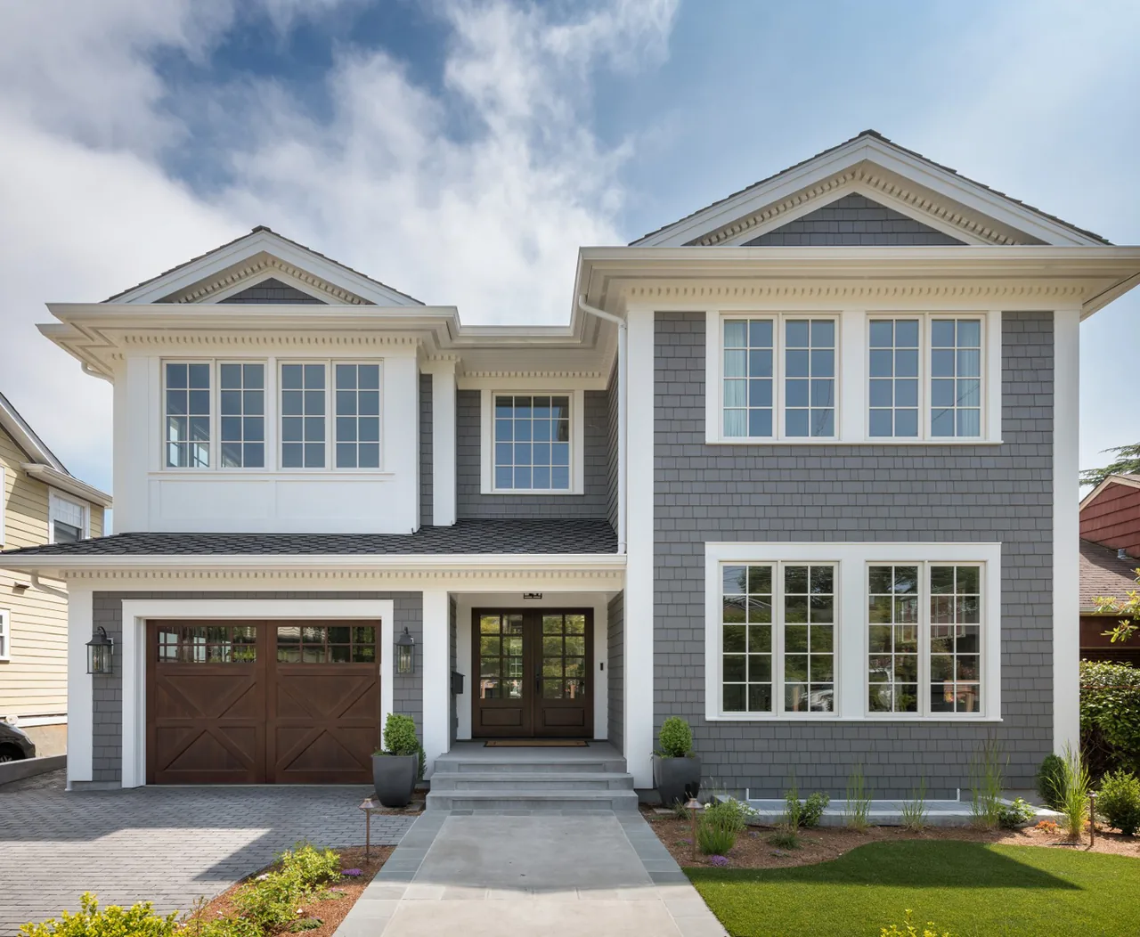 The Queen Anne Residence features gray shingle siding and a wooden garage door in its front exterior design.