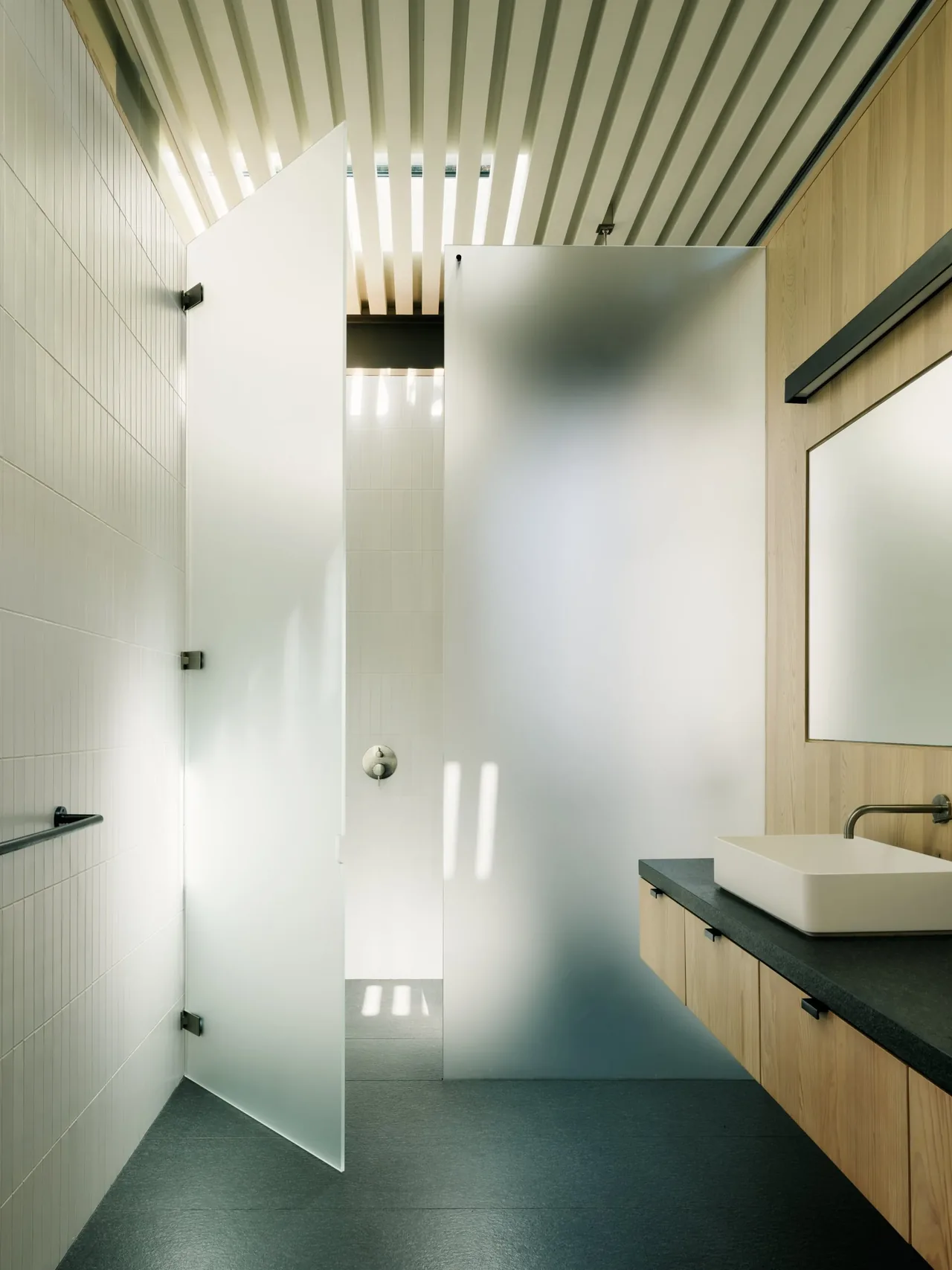 Bathroom featuring frosted glass shower doors, wood-paneled walls, and a floating vanity with a rectangular sink and dark countertop.
