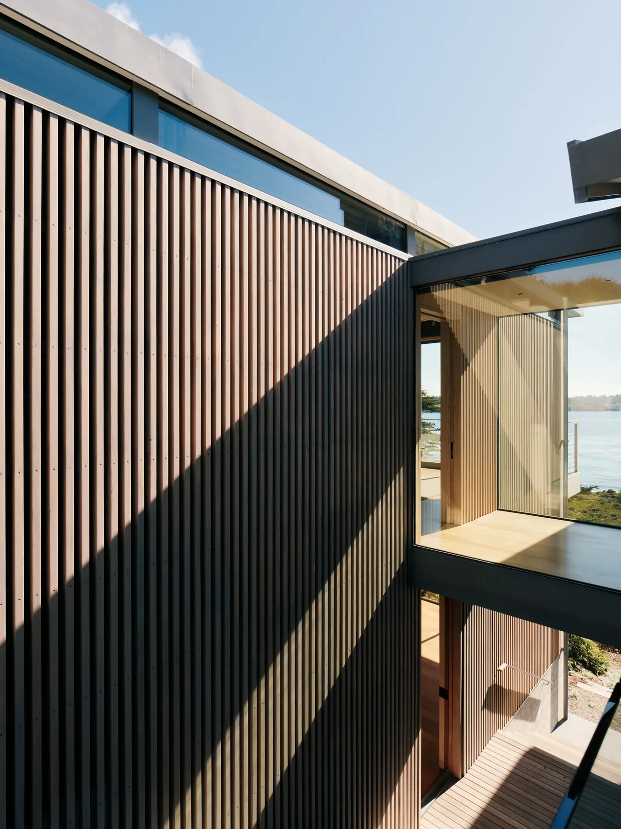 Modern house exterior features vertical wood slats and a cantilevered glass corridor with coastal views.