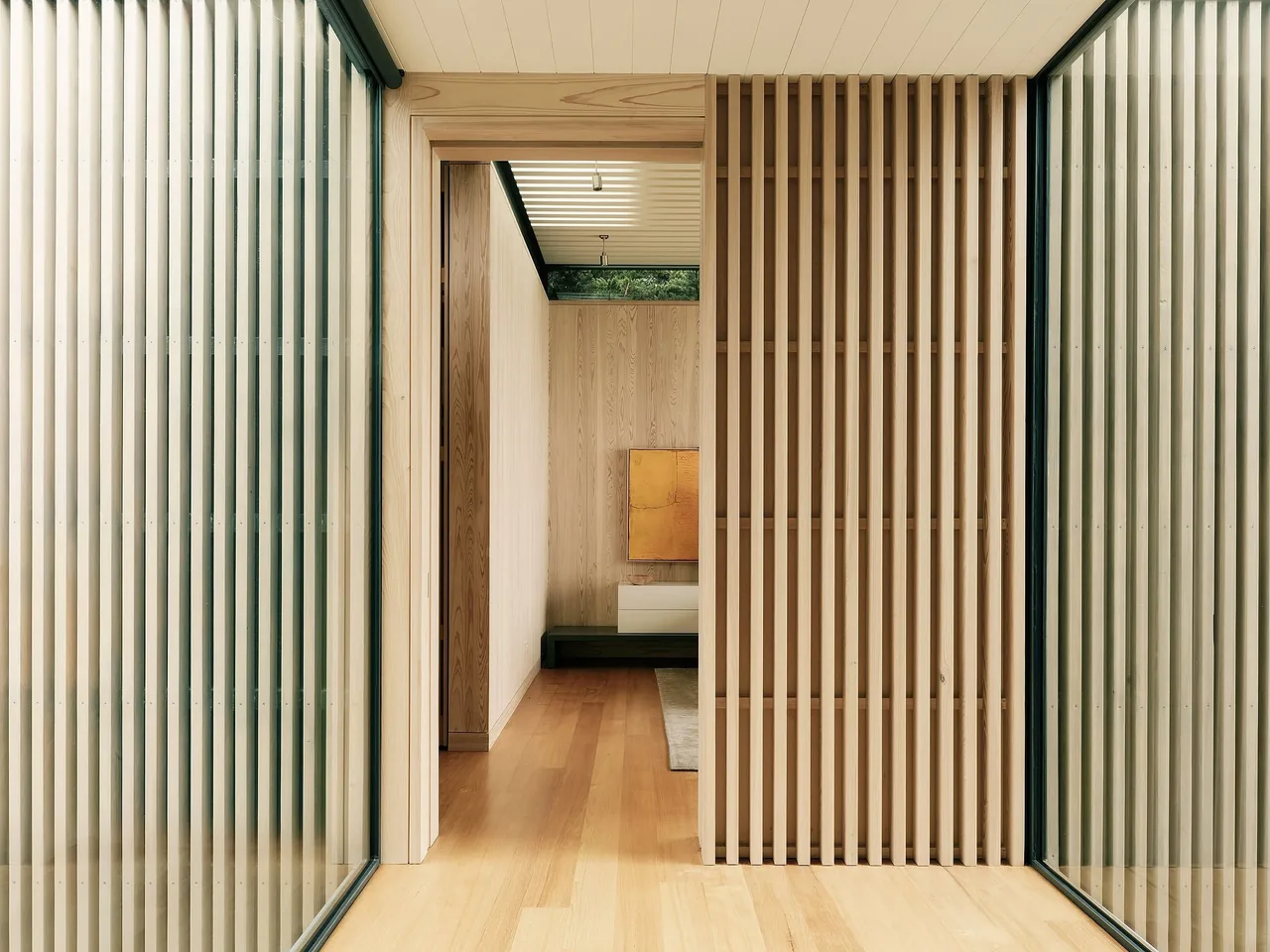 The hallway features vertical wood slats, floor-to-ceiling glazing, and a light wood floor with a slatted ceiling above.