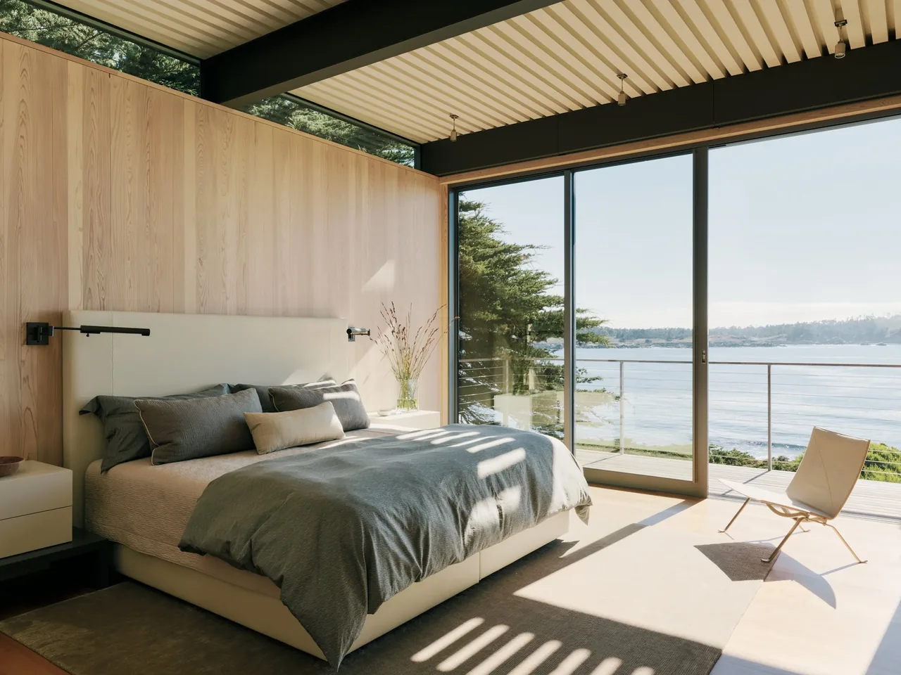 Bedroom with floor-to-ceiling glass doors and light wood paneling overlooking a coastal view.