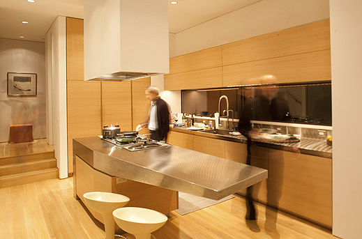 The Wei Residence kitchen features wood cabinetry, stainless steel island, and recessed downlights in an open plan.
