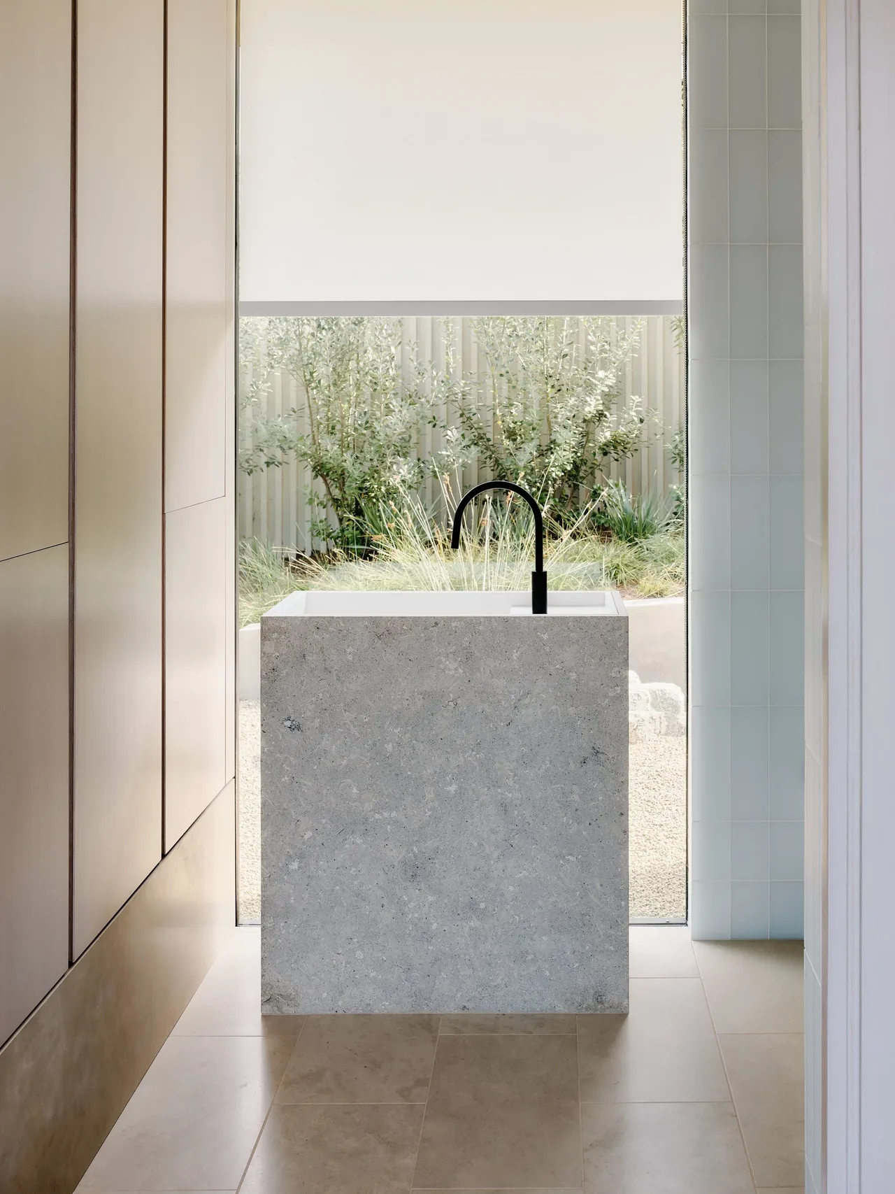 Kitchen island made of stone with a black faucet, positioned near a large window with landscaping view.