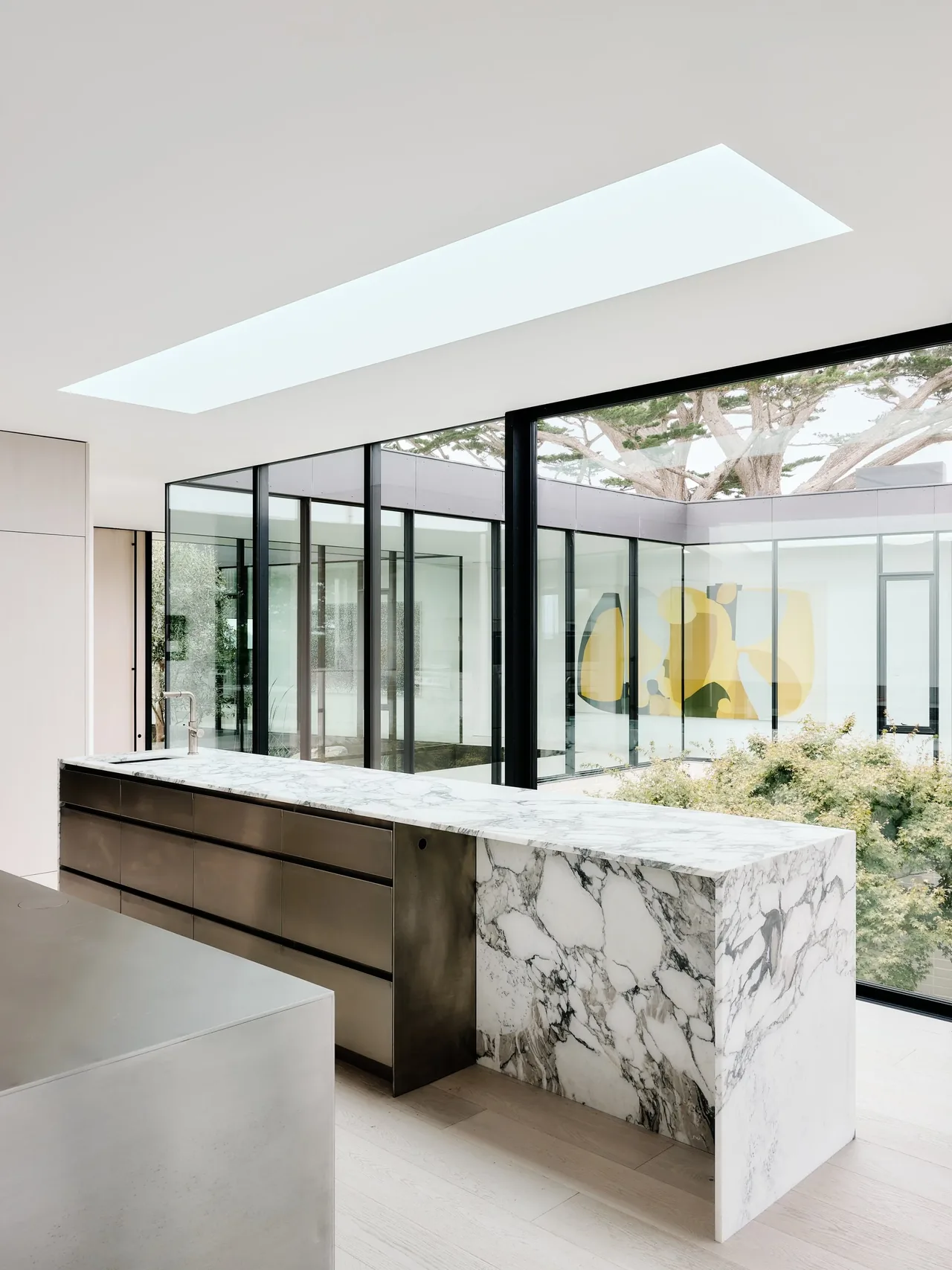 Kitchen interior featuring a marble island and black metal drawers with floor-to-ceiling windows to a courtyard.