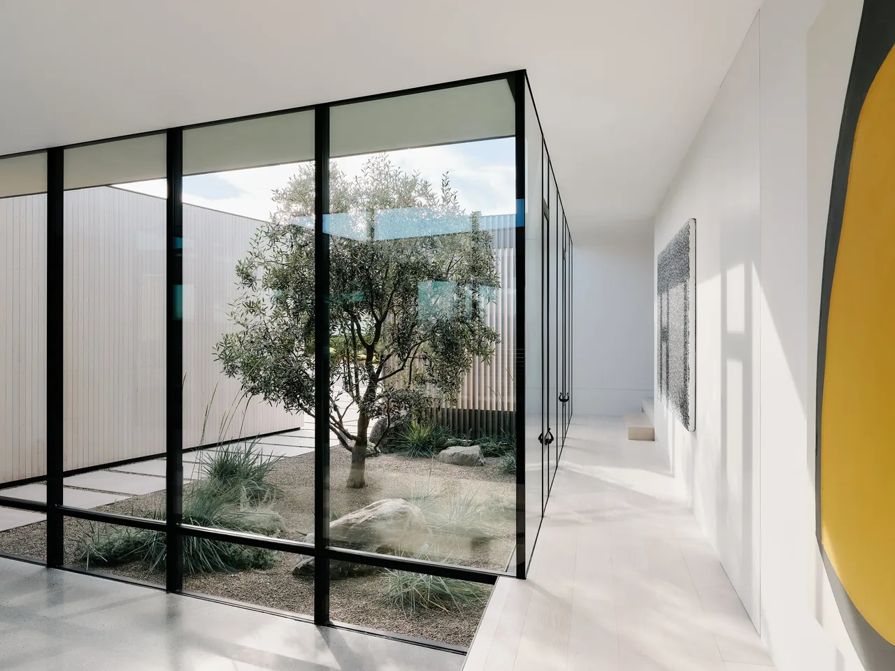 Hallway with floor-to-ceiling glazing connecting to a minimalist courtyard with sparse landscaping.