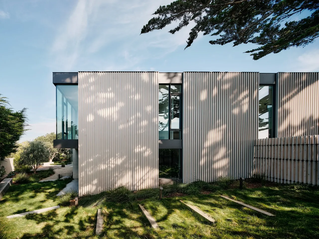 Modern home exterior at Carmel Meadows with vertical wood siding and narrow windows reflects surrounding trees in early evening.