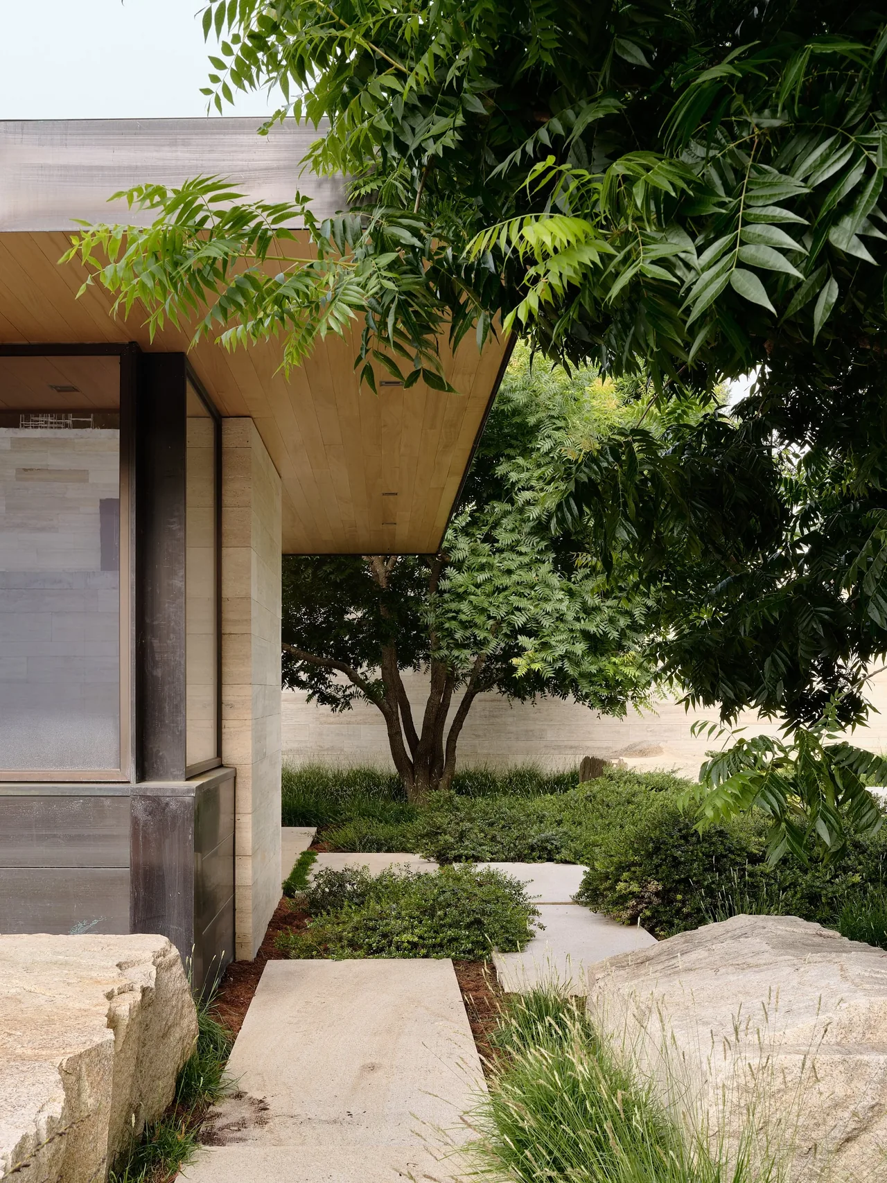 Modern home's exterior with stone steps leading to the entrance under a wood soffit surrounded by landscaped greenery.